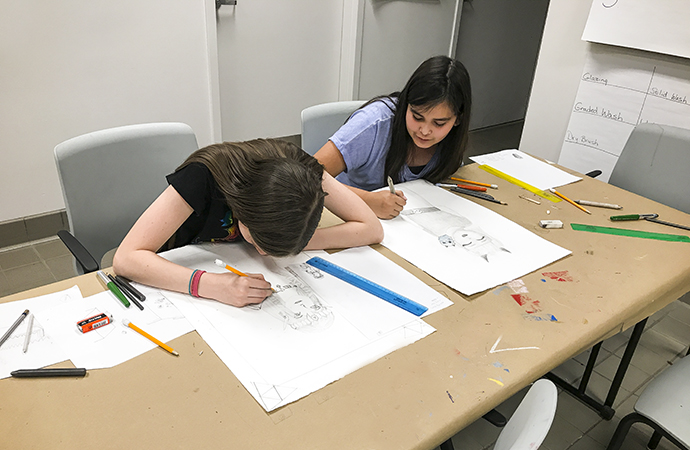 Two art students draw on some paper.