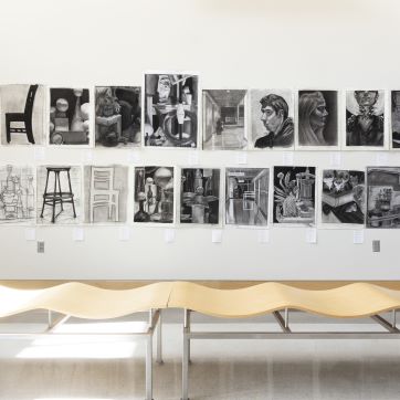 A bench in front of black and white pencil drawings on display