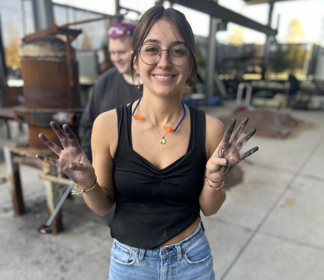 Student smiling holding up sooty hands after working the sculpture studio.