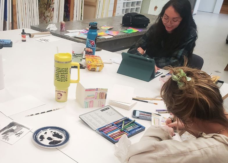 Two smiling student collaborate during a book arts class.