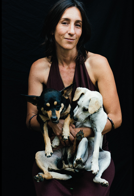 Person holding a black dog and a white dog in front of a black background.