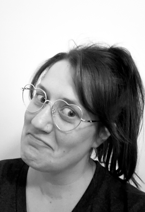 Black and white head shot of dark-haired female with heart-shaped glasses and a hoop nose ring.