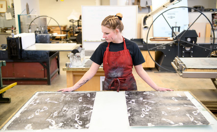 An artmaker looks at a printmaking canvas.