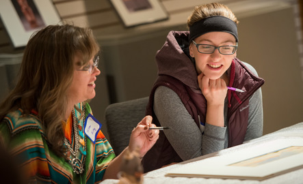 Two UW community members sit at a table and actively discuss the art in front of them at a UW Art Museum event.