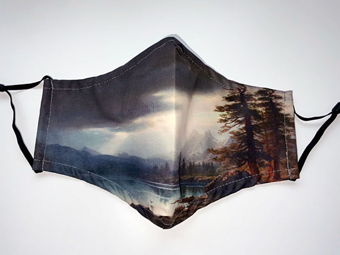 Landscape painting printed on a face mask. Majestic sunlight beaming through clouds. Grand Teton mountains in background, lake in foreground, large pinetrees on the right