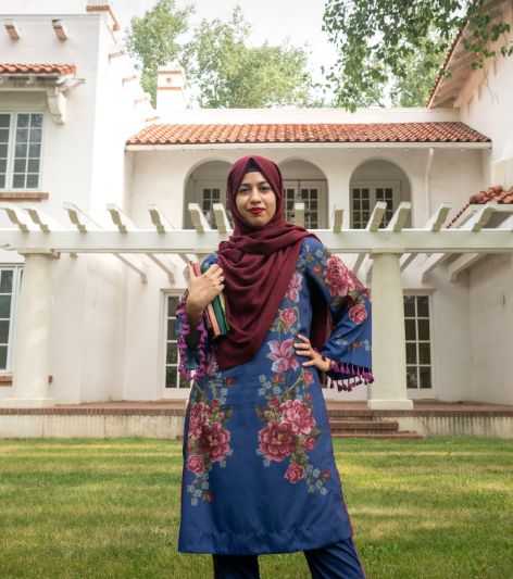 A student smiles and holds a book while outside the Cooper House on campus