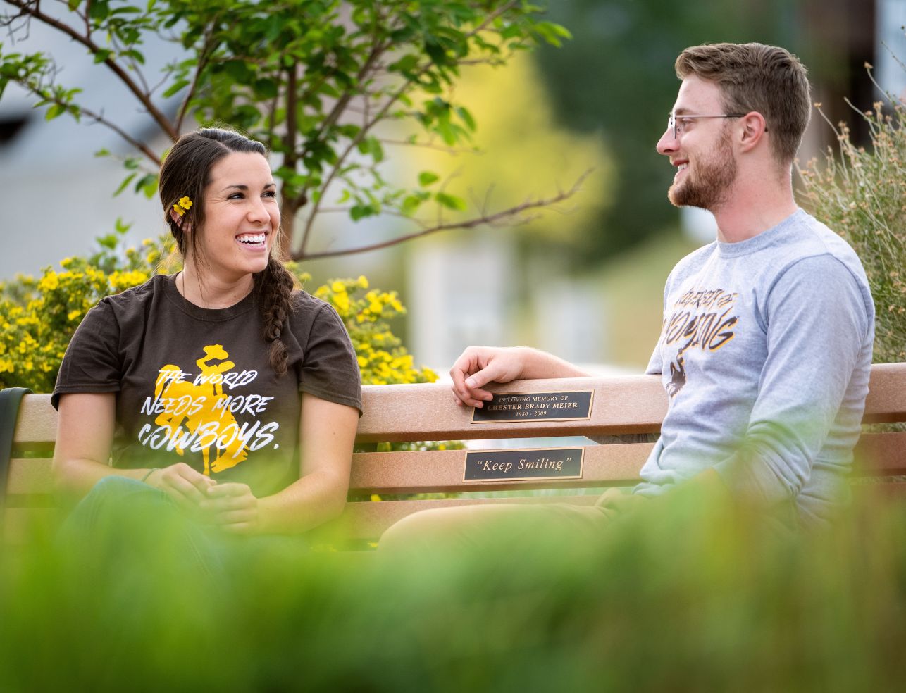Two students talk to each other and laugh on a bench outside the Visual Arts Building. 