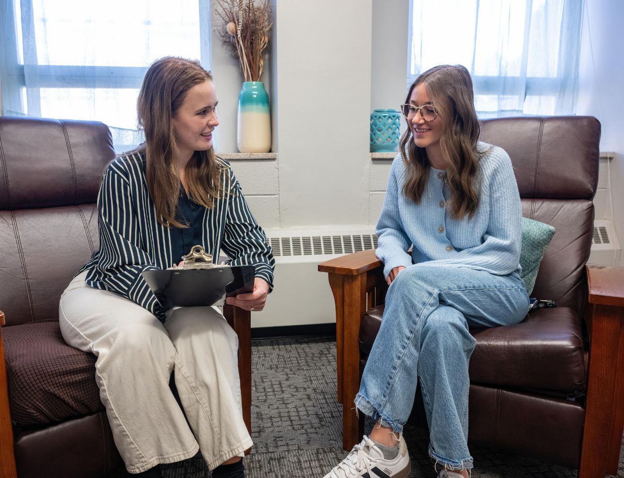 Two female students smile while talking to each other in an office.