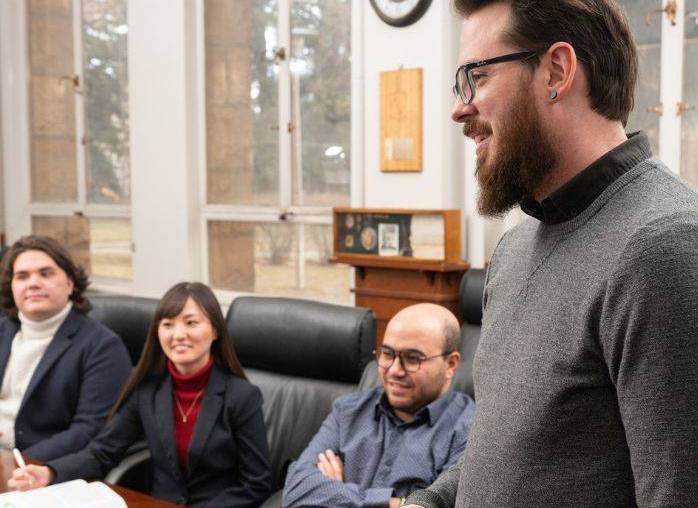 A group of students and faculty members have a discussion around a table. 