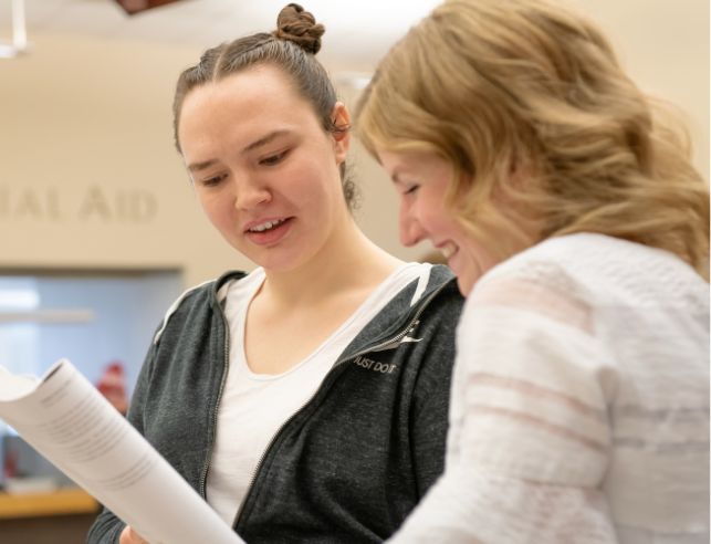 Two women look at a piece of paper together. 