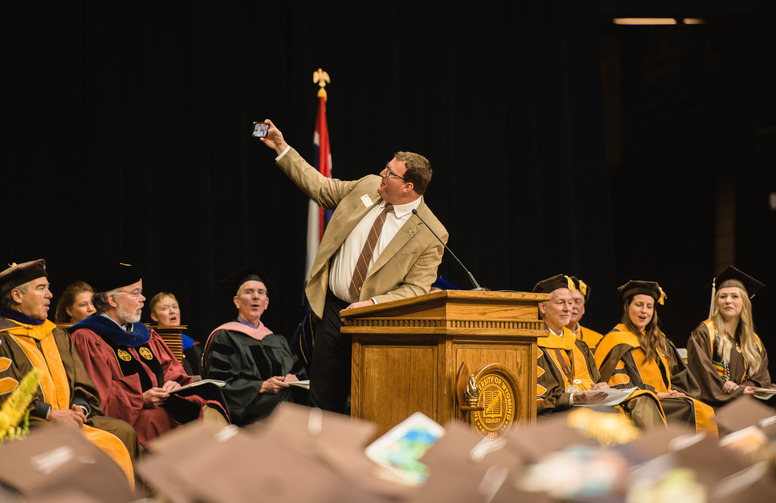 Speaker at commencement podium takes a picture with the crowd.