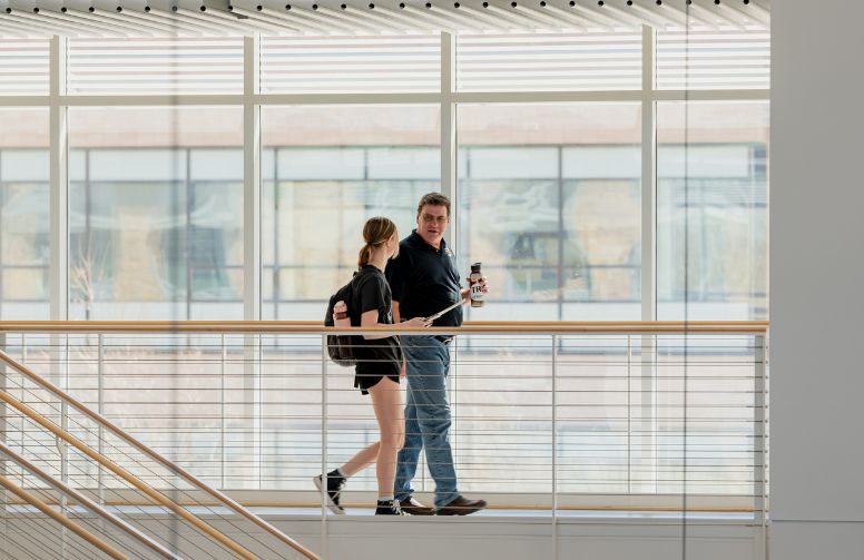 A student walks through a campus building with a mentor.