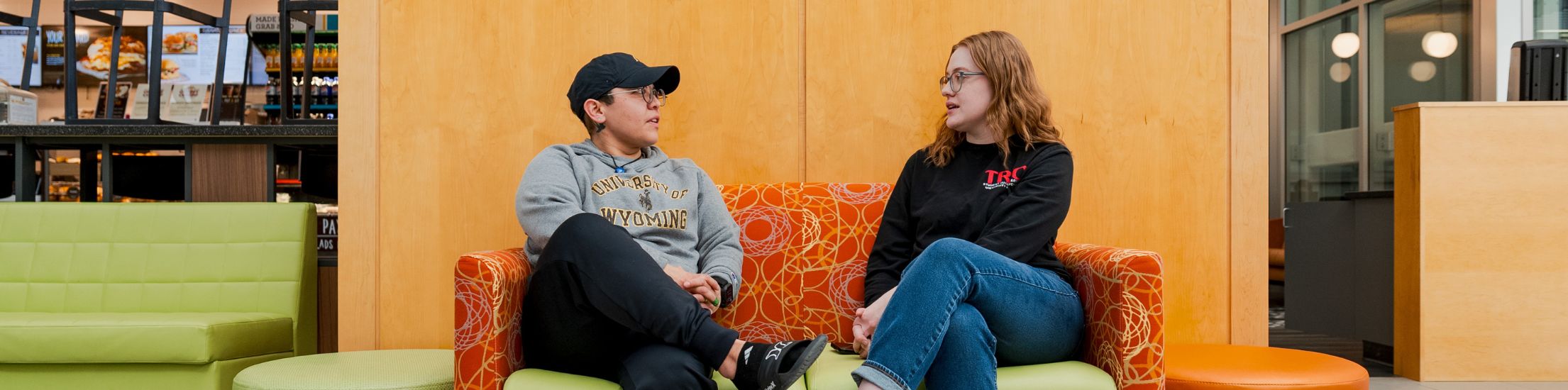 Two individuals sit on a bench and talk.