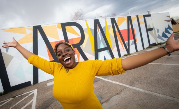 A student smiles and holds up her arms outside the Laramie mural on 3rd Street.