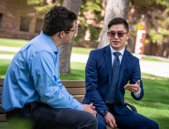 Two students discussing, sitting on bench