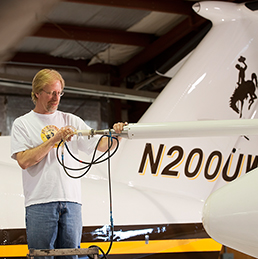 Person handling nose boom instrument with aircraft in background