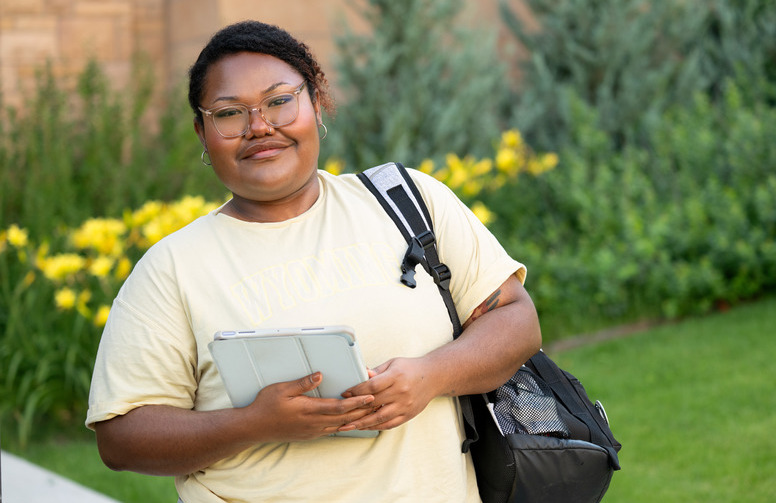 student smiling at camera with her backpack and tablet