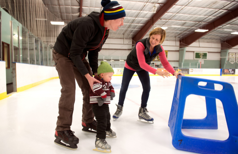 two adults help a small child ice skate
