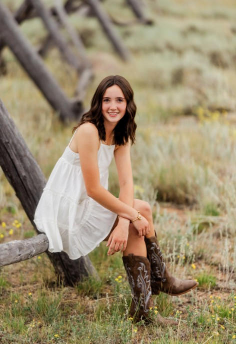 Smiling woman with white dress sitting on a rail fence in a field with sage and wildflowers..