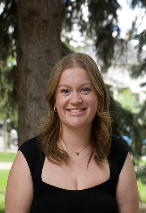 Smiling woman in a black shirt with a pine tree in the background.