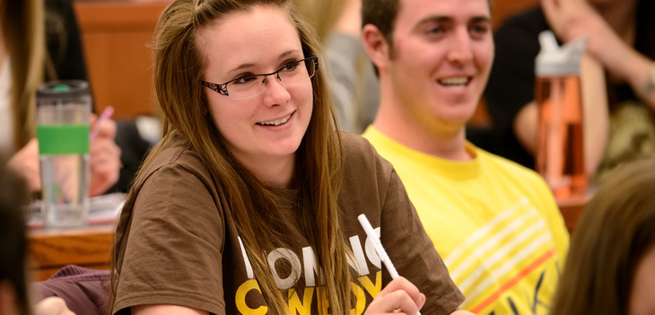 A student smiling in class while taking notes