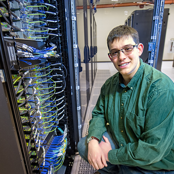 student poses next to supercomputer