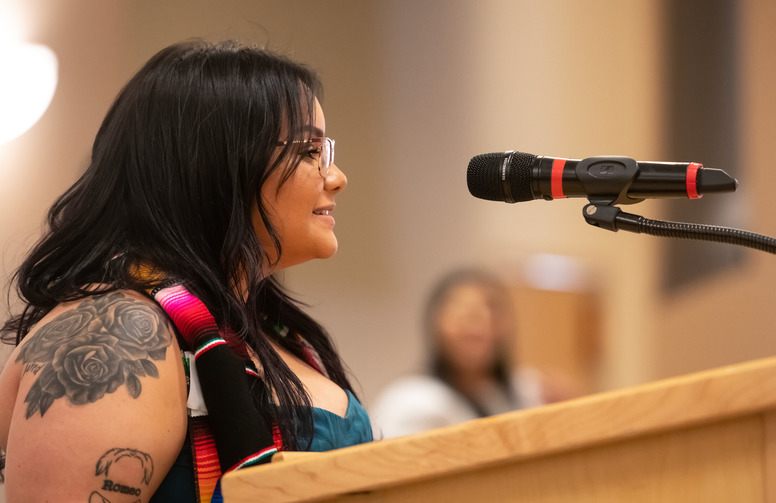 A student with a tattoo on their shoulder speaks at a podium.