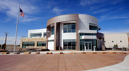 The NCAR Super Computing Center in Cheyenne pictured on a blue sky day with the American flag flying next to it.