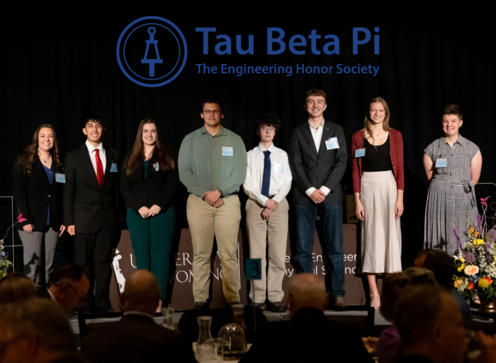 Group of male and female students standing on a stage in front of an audience, black background
