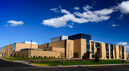 The High Bay Research Facility on a blue sky day with a couple clouds overhead and green grass out front.