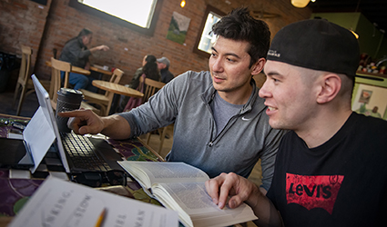 Two males sitting in cafe look at laptop computer screen