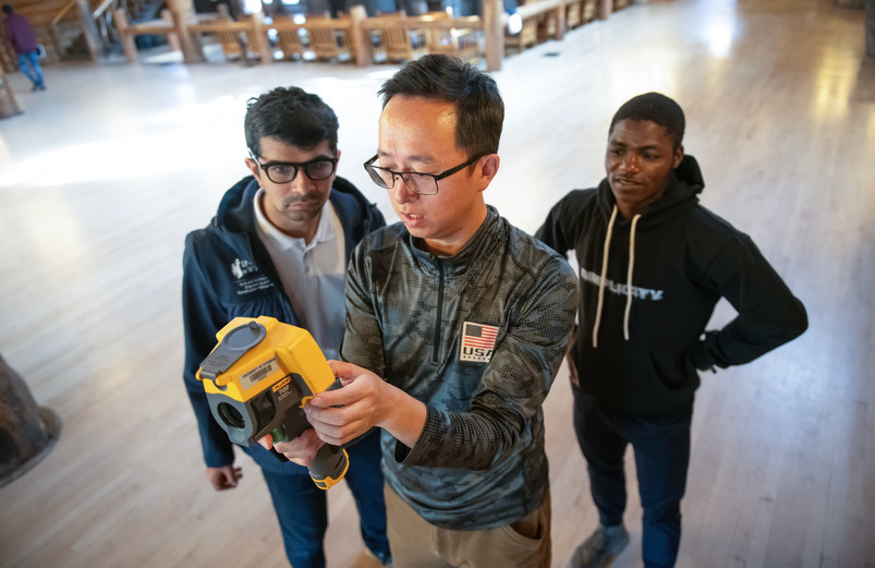 Three male students looking at a piece of equipment