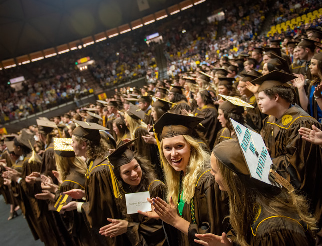 Students at a UW commencement ceremony stand and clap