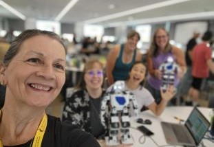 Smiling teacher in foreground with classmates sitting at tables behind