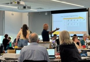 teacher pointing at digital image on screen in classroom with seated adult students