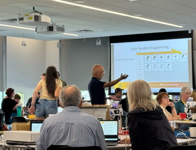 teacher gesturing to digital screen in front of class of adult students