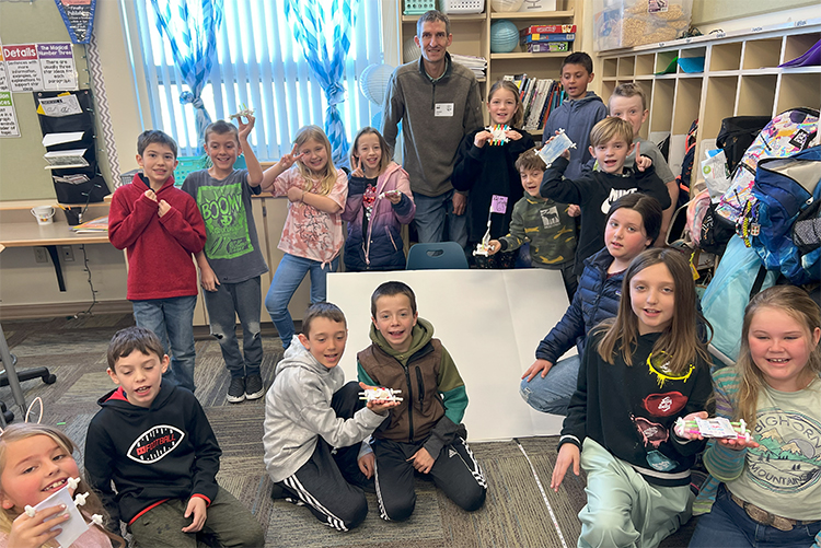 A professional land surveyor teaching a group of young students.