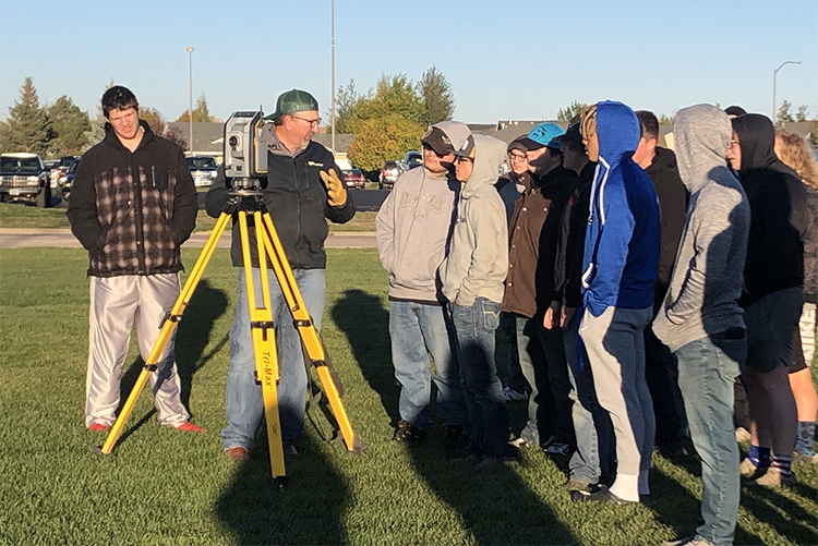 A professional land surveyor teaching a group of young students.