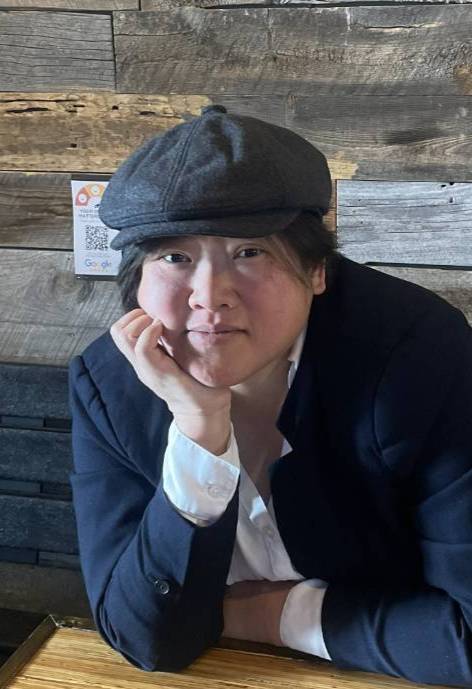 Kim Lau sits at a table and rests her chin on her hand, smiling at the camera.