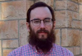 Dr. Andrew Parsekian, wearing a blue button up shirt, green jacket, and glasses, smiles at the camera