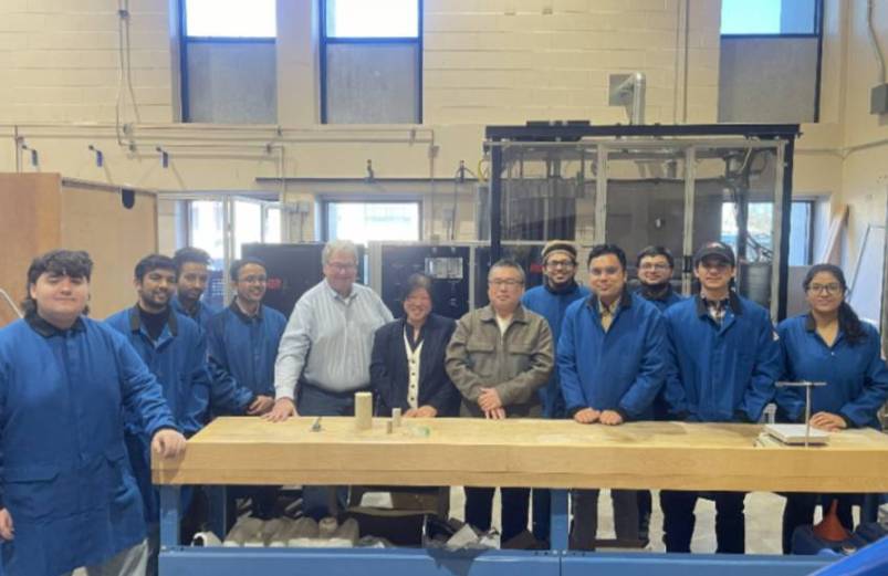 Dr. Kam Ng, Dr. Anthony Denzer, and Chooi Kim Lau pose in the Geomaterials Research Lab with grad students. All people are lined up and smiling at the camera.