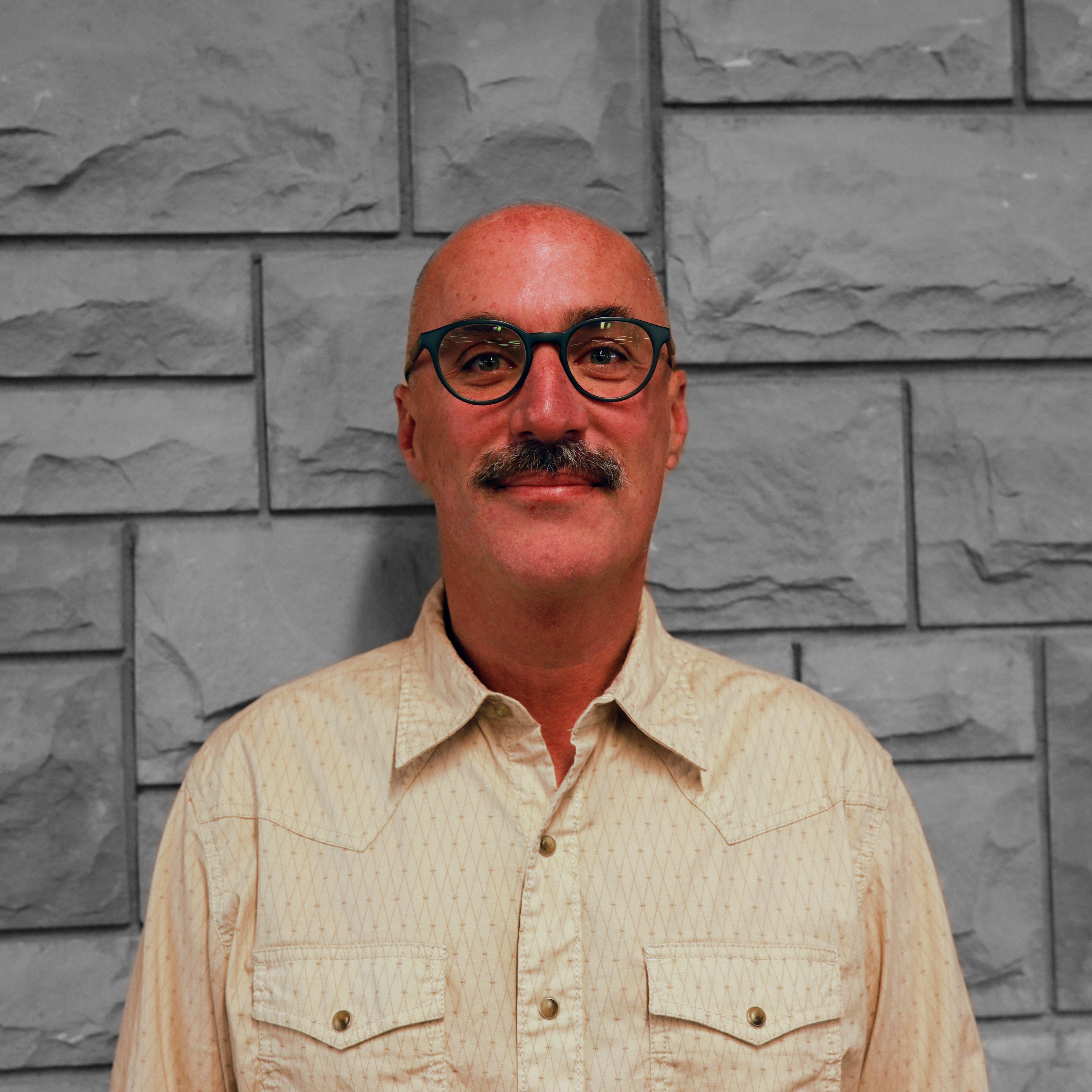 Image of faculty member Paul Gregory standing in front of a grey scale brick wall 