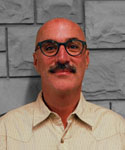 Image of faculty member Paul Gregory standing in front of a grey scale brick wall