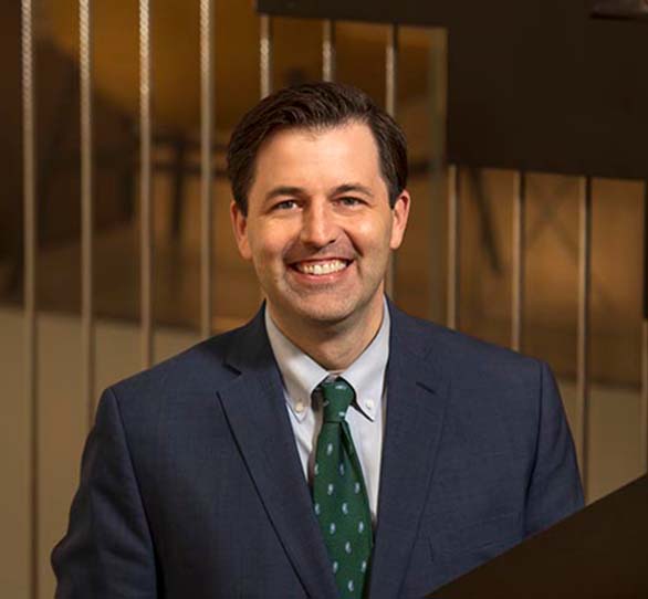 a white male gives a toothy smile while wearing a blue suit and green tie