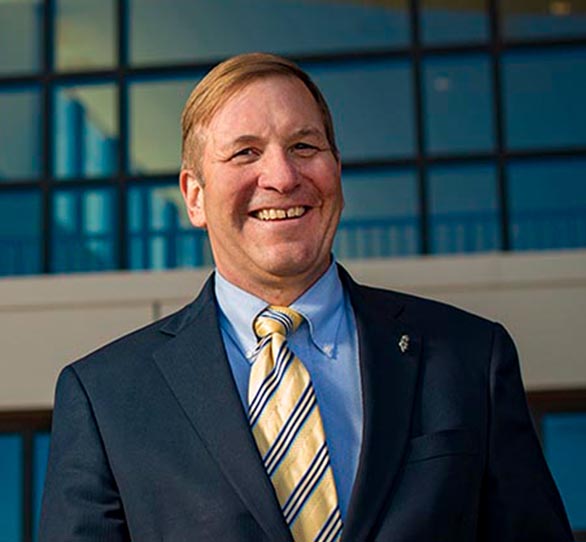 a white male wears a blue suite and yellow tie in front of a University Wyoming building