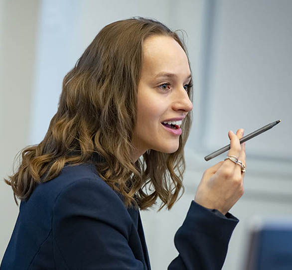 A woman in a blue blazer holds a pen in her hand with her mouth agape.