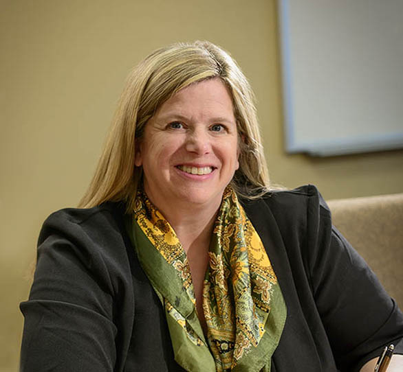 a woman wears a black blazer and colorful scarf and looks into the camera while sitting