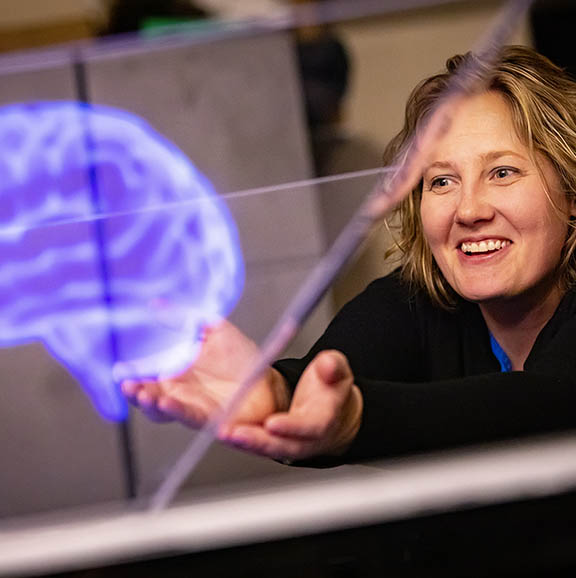 A woman pretends to hold a virtual reality brain image while smiling