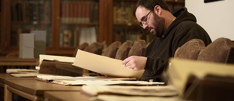 a man with a beard looks at a book while sitting at a table in the library