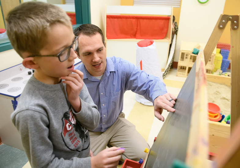 Adult teaching a child at a chalkboard – A man points at the board while a boy listens closely.